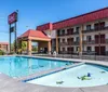 An outdoor swimming pool is featured in front of a multi-story motel with a large signboard under a clear blue sky