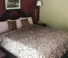 The image shows a neatly made bed with patterned bedding in a bedroom with a burgundy accent wall a two-tone paint job and a framed picture above the bed