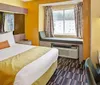 The image shows a brightly colored hotel room with a large bed a window seat and a patterned carpet