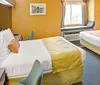 The image shows a brightly colored hotel room with a large bed a window seat and a patterned carpet