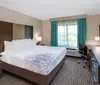 The image shows a neatly arranged modern hotel room with a large bed a work desk and a flat-screen TV