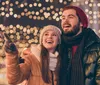 A joyful couple is enjoying a festive night out surrounded by sparkly lights while the woman points at something interesting outside the frame
