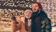 A joyful couple is enjoying a festive night out, surrounded by sparkly lights, while the woman points at something interesting outside the frame.