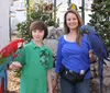 A young person and an adult are posing with a colorful red macaw and a blue hyacinth macaw perched on their arms