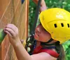 A young person wearing a yellow helmet is focused while climbing a wooden wall with green handholds