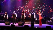A group of performers are singing on stage under colorful stage lighting.