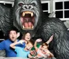 A family is posing with exaggerated expressions of fear as if they are being attacked by a large gorilla in what looks to be a staged amusement park photo opportunity