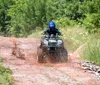 A person wearing a helmet and protective gear is riding an ATV on a narrow dirt trail through a forest