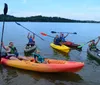A group of smiling people are seated in colorful kayaks holding paddles and appear ready for a paddling adventure on a calm lake