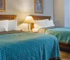 The image shows a neatly arranged hotel room with two beds covered in turquoise bedspreads wooden headboards a shared nightstand with a lamp and tasteful wall art