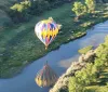 A colorful hot air balloon floats above a serpentine river casting a reflection on the water as it flies over a lush landscape