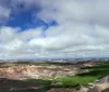 The image shows a panoramic view of a rugged landscape with layered rock formations green valleys and a vast sky dotted with clouds