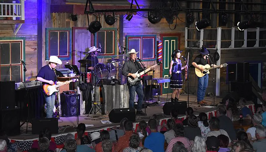 A band performs on stage in front of an audience in a venue decorated with rustic, wooden facades.