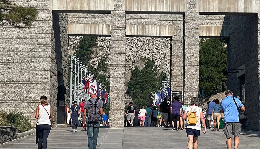 Visitors are walking towards an entrance flanked by rows of flags, leading to a monument or park.