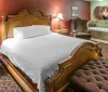 The image is of a luxurious hotel room featuring a large bed with an ornate headboard traditional furnishings and an open-concept bathtub within the room
