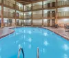 An indoor swimming pool is surrounded by two floors of balconies with several rooms looking out onto the pool area complete with poolside seating and a warm inviting ambiance