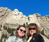 Two people are posing for a photo in front of the Mount Rushmore National Memorial which features the carved faces of four US presidents