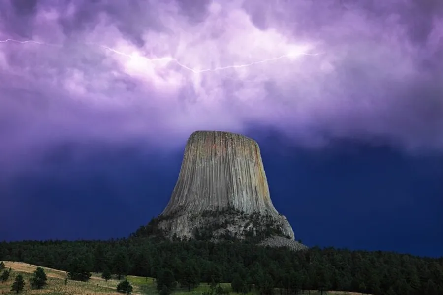 A striking butte rises prominently against a dramatic sky illuminated by lightning.