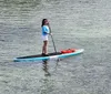 A person is stand-up paddleboarding on calm water with a life jacket secured to the front of the board