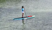 A person is stand-up paddleboarding on calm water with a life jacket secured to the front of the board.