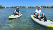 Two individuals are enjoying a sunny day out on the water, each leisurely pedaling a sit-on-top kayak.