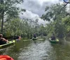 A group of people are kayaking through a serene waterway surrounded by lush greenery under a partly cloudy sky