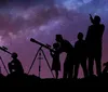 A group of silhouetted people including children and adults are stargazing with telescopes under a starry night sky