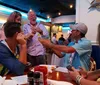 A group of people is sharing a joyful moment at a restaurant with one man playfully tipping a large drink towards another while everyone laughs
