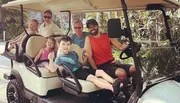 A group of people, including adults and children, are smiling and posing for a photo in a golf cart.