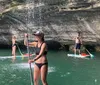 A group of people are paddleboarding near a waterfall and a rocky cliff
