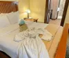 The image shows a neatly made hotel room bed with a white bathrobe laid out on it a gift bag on the side and a glimpse of an en-suite bathroom and entryway in the background