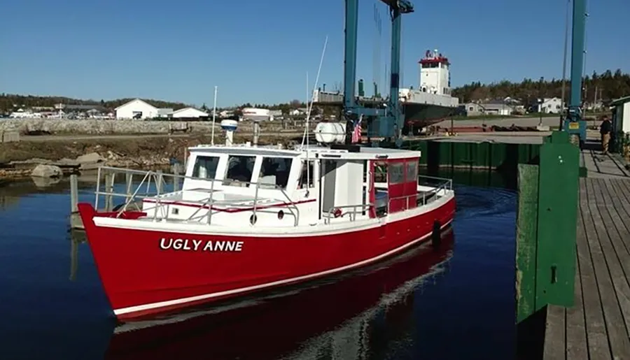 A red and white boat named UGLY ANNE is moored at a wooden dock on a clear day.