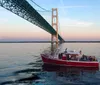 A tour boat named Ugly Anne is cruising near a large suspension bridge during a calm evening