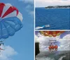 A person is parasailing under a blue and red parachute against a backdrop of a clear sky with a few clouds