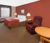 The image shows a neatly arranged hotel room with a king-sized bed a red accent wall contemporary furnishings and a view outside through a glass door