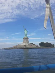 This is a daytime photo featuring the Statue of Liberty viewed from a boat, with clear skies and a section of the boat's rigging visible in the frame.