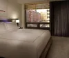 A modern hotel room with a large bed offers a panoramic view of a city skyline through its window