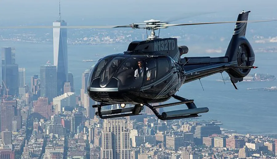 A helicopter with passengers on board is flying over an urban cityscape with skyscrapers in the background.