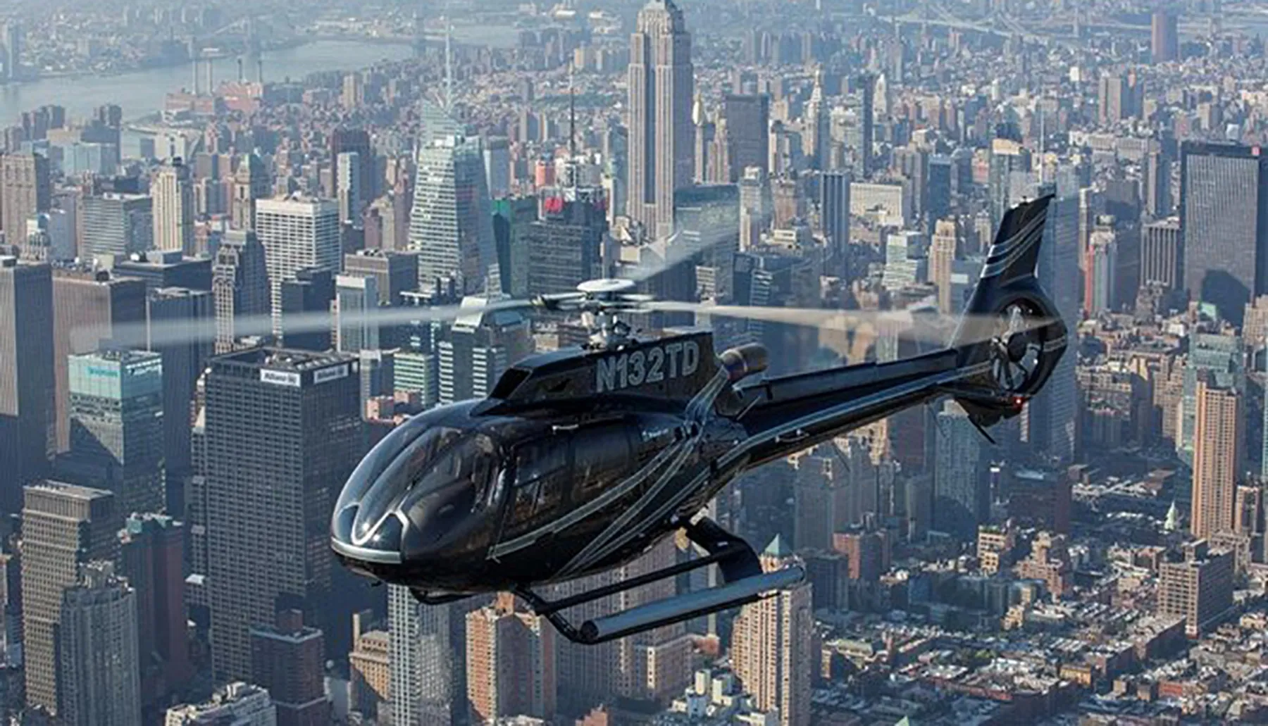 A helicopter is flying over a densely built urban area, showcasing a city's skyline in the background.