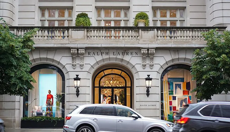 The image shows the facade of a Ralph Lauren store with an elegant archway and window displays, and a passing car is partially visible in the foreground.