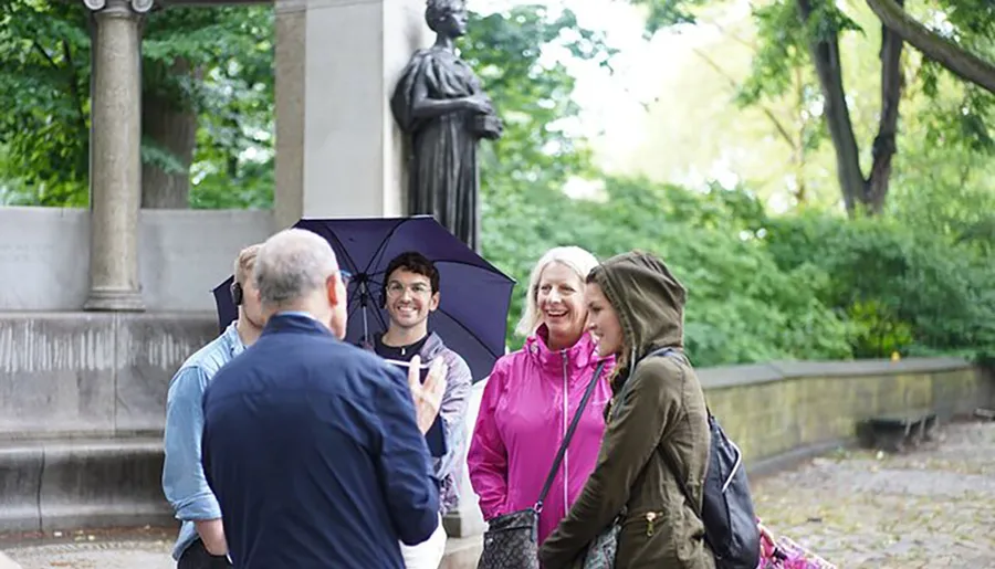 A group of people, one holding an umbrella, appear engaged and smiling during an outdoor conversation.