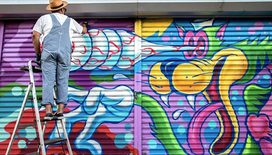 An artist is standing on a ladder while creating vibrant graffiti art on a roller shutter.