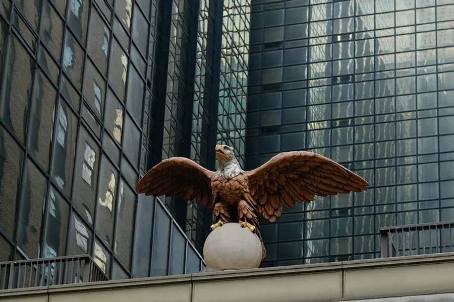An eagle statue with outstretched wings perched atop a pedestal against the backdrop of a modern glass skyscraper.