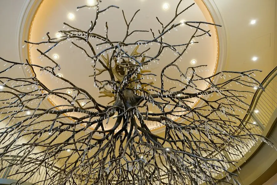 The image shows a large, intricately detailed tree sculpture with sprawling branches, located inside a room with a curved ceiling and soft lighting.