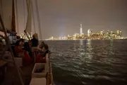 People are enjoying a nighttime sail with a view of a brightly lit city skyline in the background.