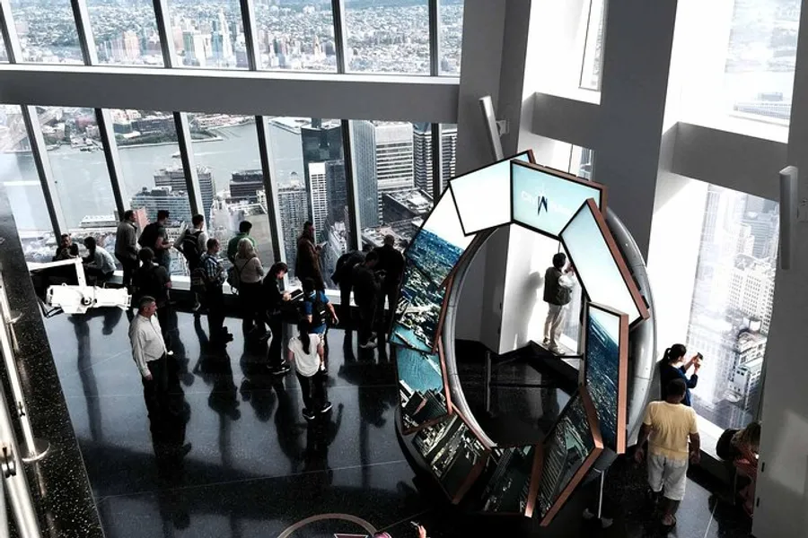 Visitors enjoy a panoramic city view from a high vantage point with large windows, while a person interacts with an installation featuring reflective surfaces.