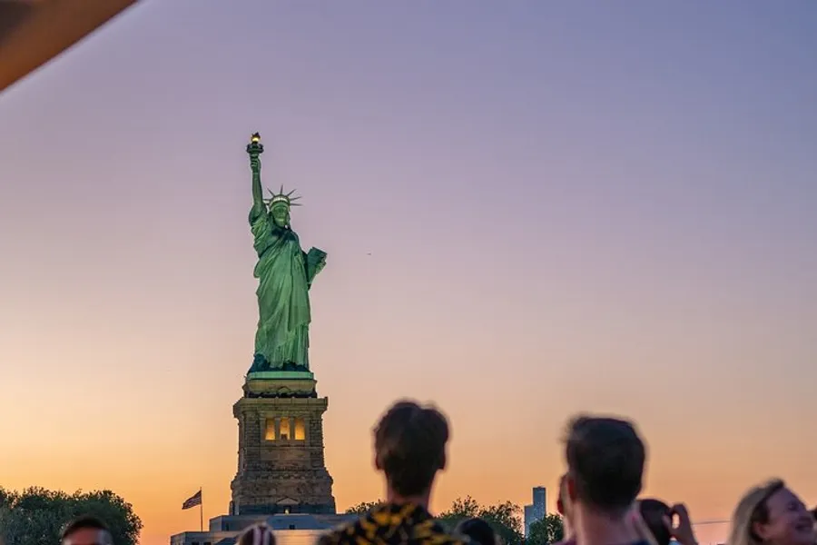 The image captures a serene evening with people gazing at the Statue of Liberty against a dusky sky.