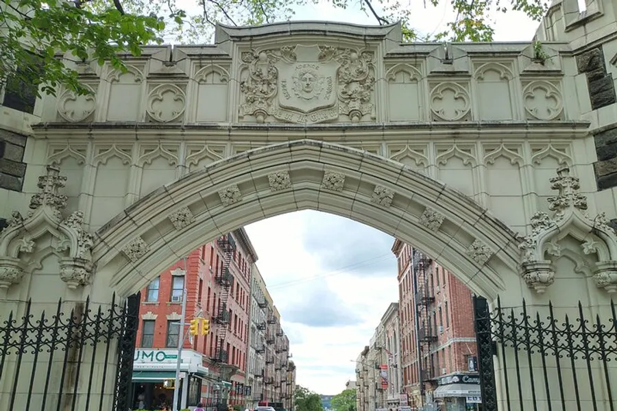 The image showcases an ornate stone archway over a street, displaying intricate carvings and a coat of arms, creating a historic atmosphere within an urban environment.