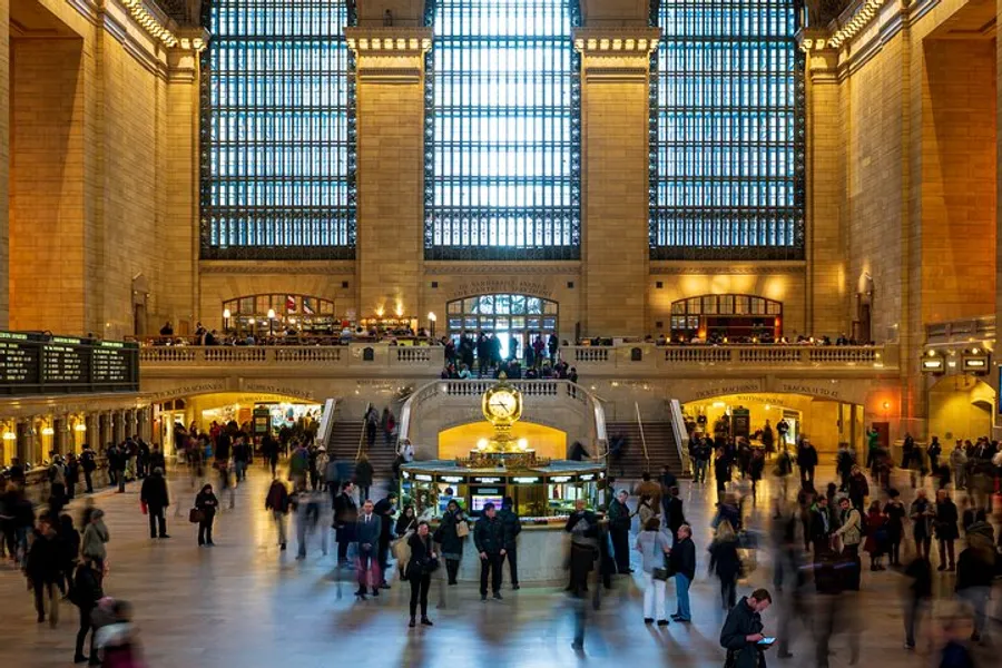 The image shows the bustling interior of a grand train station with high windows and a large clock, where people are commuting and milling about.