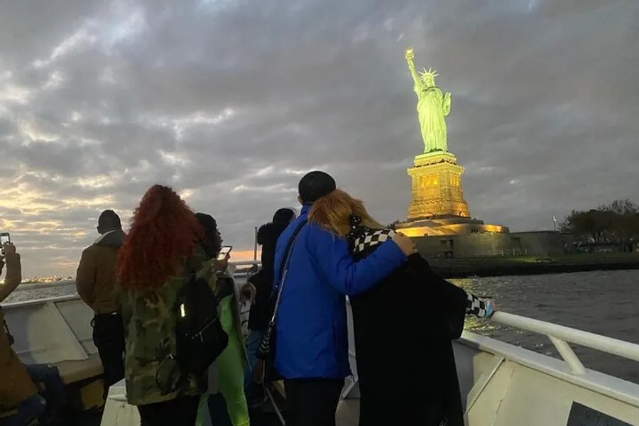People on a boat are taking photos of the Statue of Liberty at twilight.